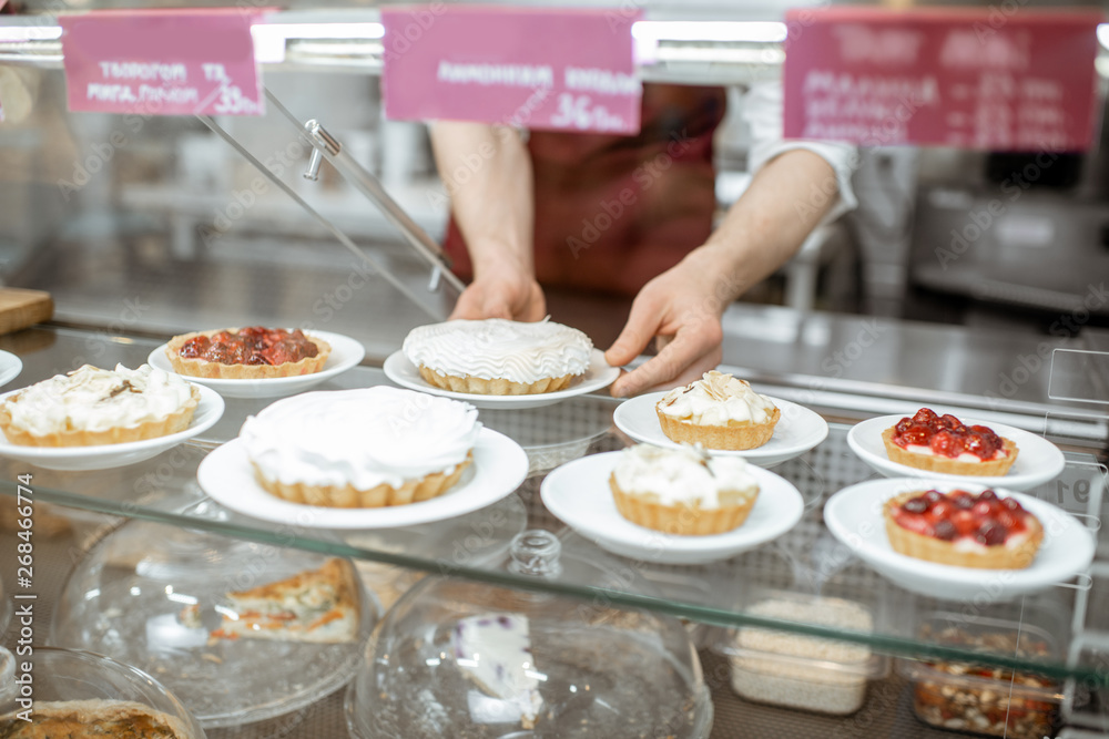 Showcase with various sweet cakes at the pastry shop and salesman on the background