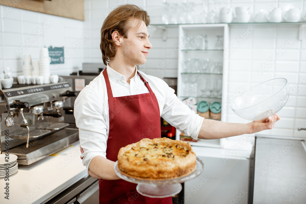 Salesman in red apron putting fresh pie into the refrigerator of the showcase at the modern pastry s