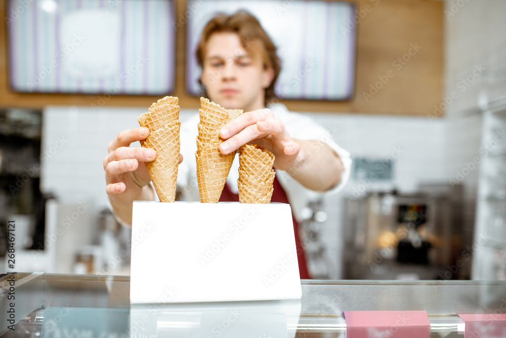 Handsome salesman taking waffle cone while making ice cream for the client in the modern pastry shop