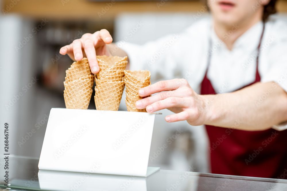 Salesman taking waffle cone while making ice cream in the modern pastry shop, close-up view