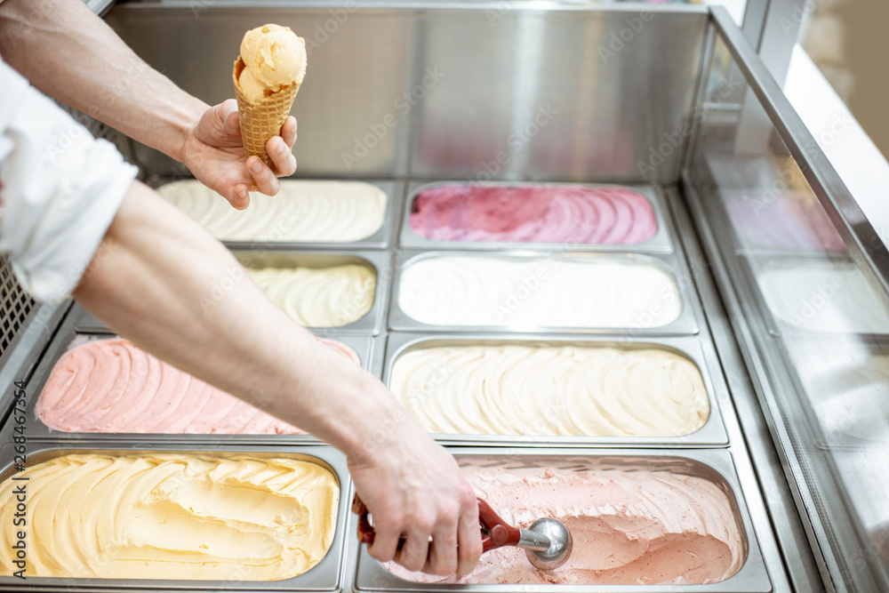 Metal trays full of colorful ice cream in the showcase refrigerator, salesman taking ice cream with 