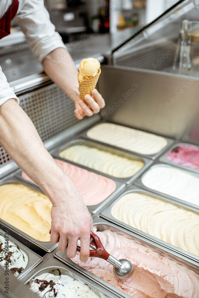 Metal trays full of colorful ice cream in the showcase refrigerator, salesman taking ice cream with 