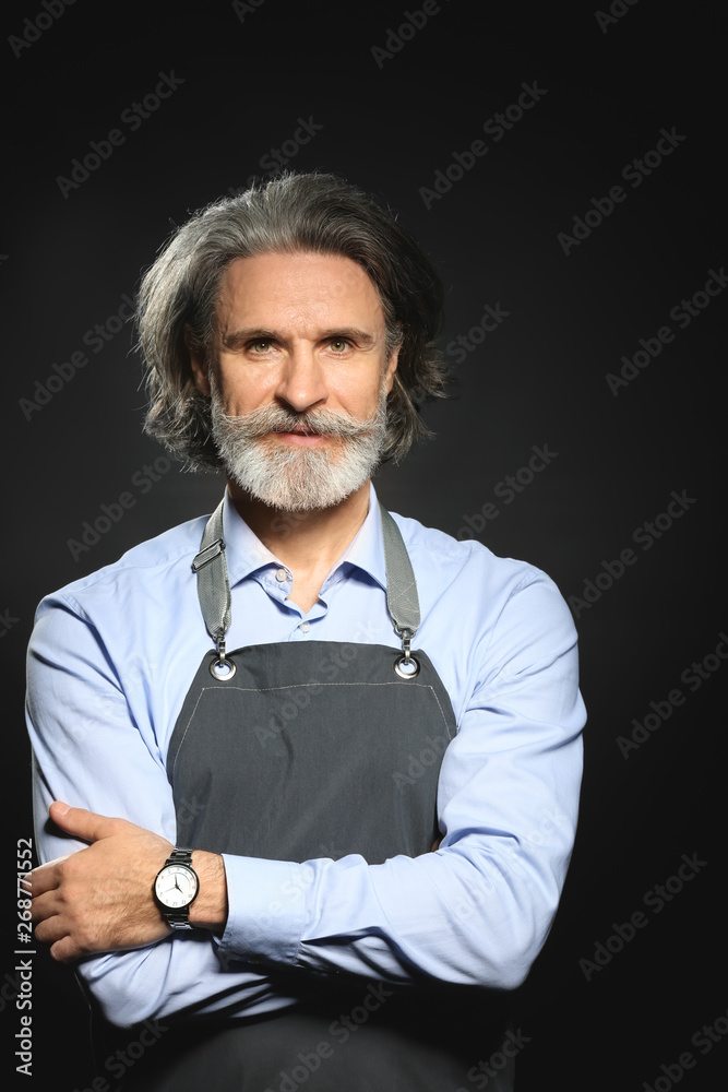 Senior man in apron on dark background