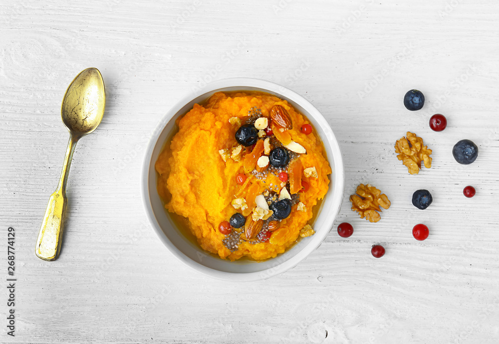 Bowl with mashed sweet potato, nuts and berries on white wooden background