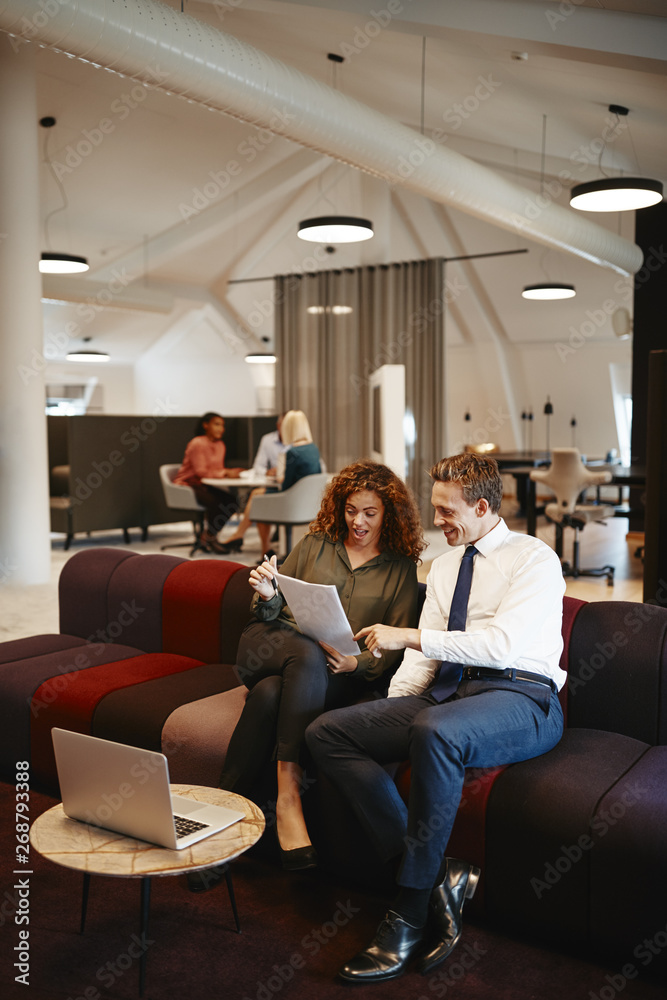 Smiling businesspeople sitting together on an office sofa discus