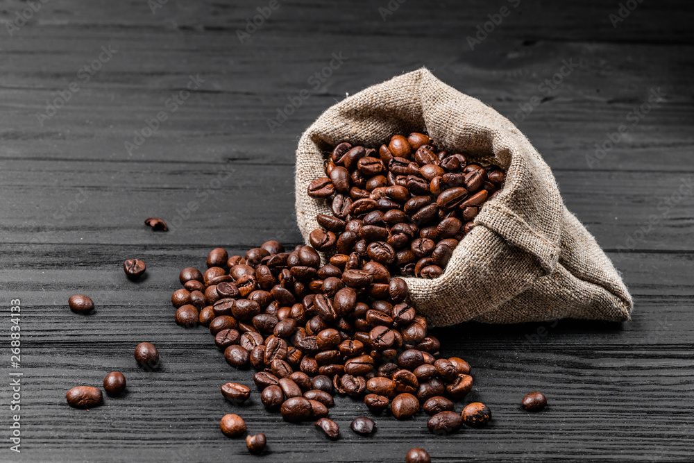 Fresh roasted coffee beans falling out the sack on the wooden surface. Brown coffee beans scattered 