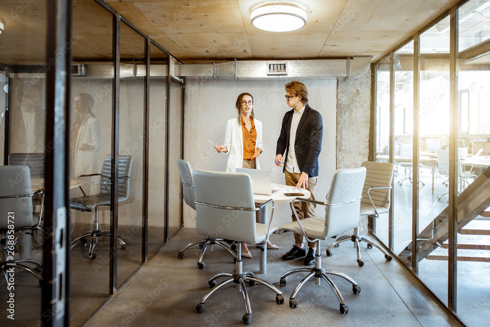 Young man and woman having a business conversation during the small conference, standing near the ro