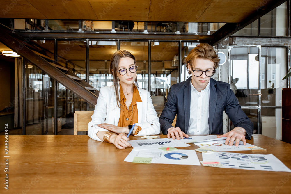 Business man and woman working with documents while sitting together at the wooden table in the offi