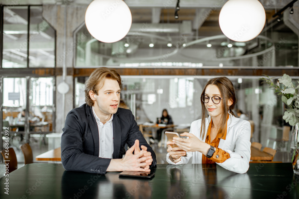 Young man and woman having business conversation while sitting together in the bar or coworking spac