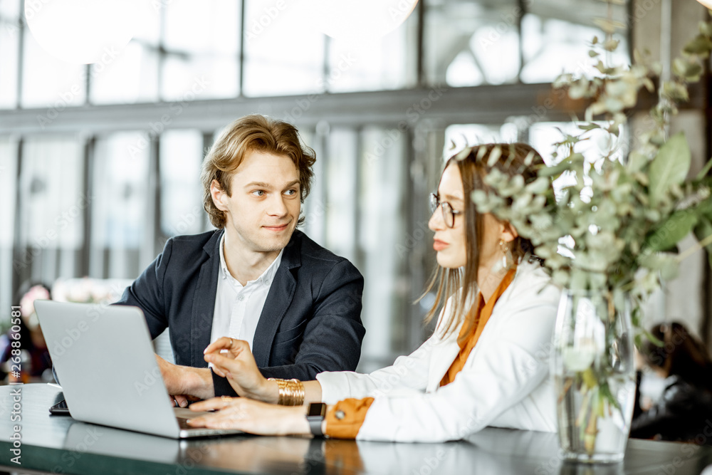 Young man and woman having a business conversation while sitting with laptop at the bar or modern sp