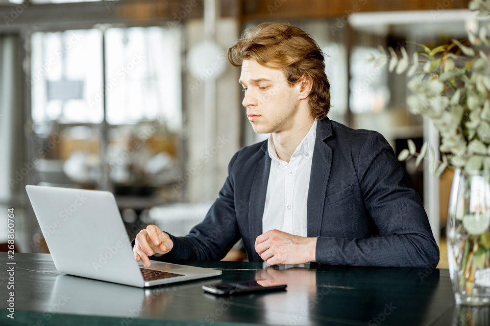 Portrait of a young handsome businessman sitting with laptop at the modern spacious bar or office