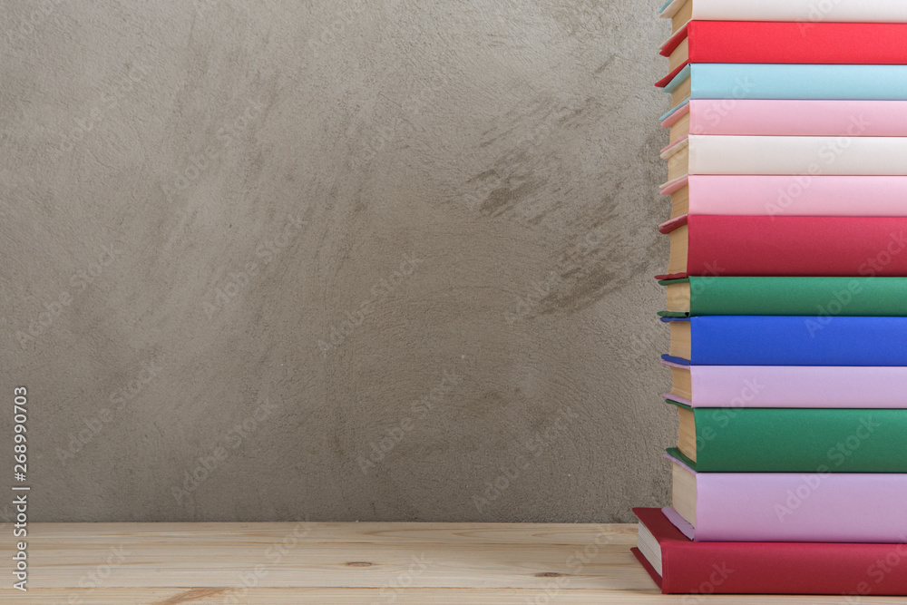 Education and reading concept - group of colorful books on the wooden table, concrete wall blackboar