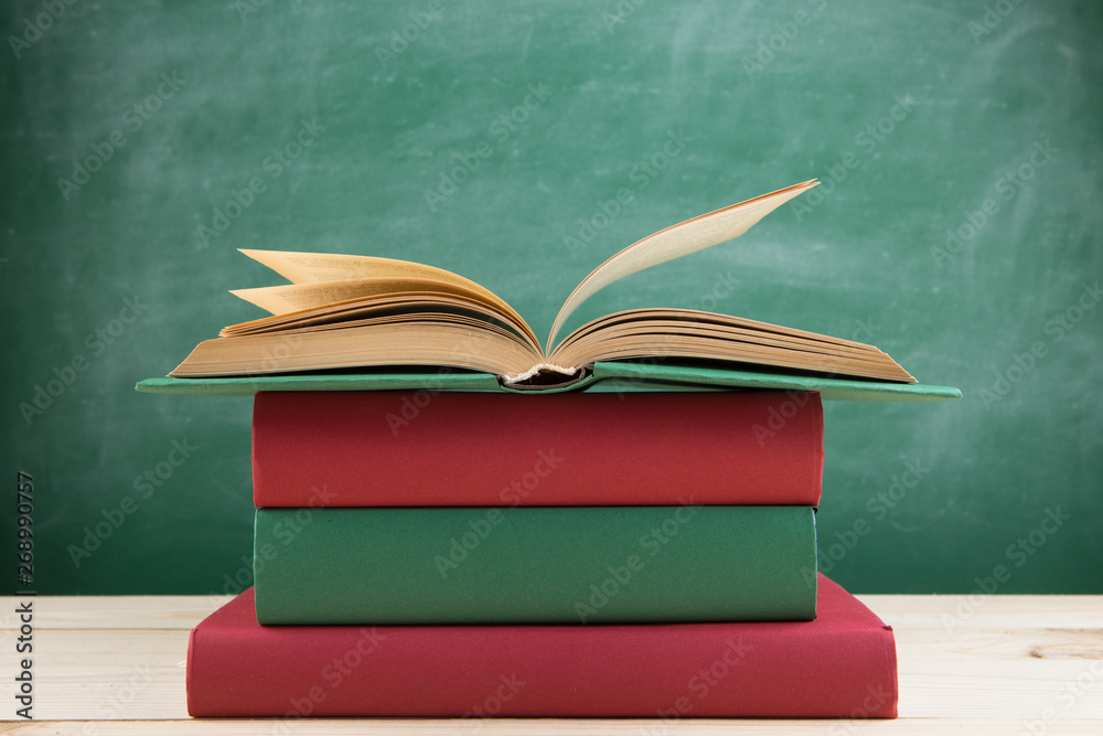 Education and reading concept - group of colorful books on the wooden table in the classroom, blackb