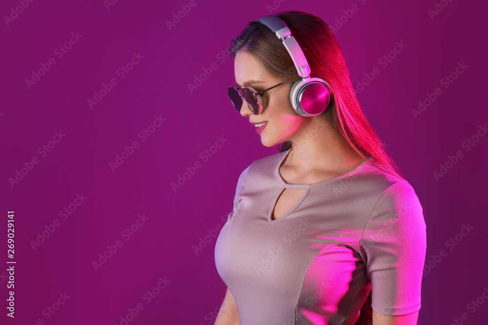 Beautiful young woman listening to music against color background