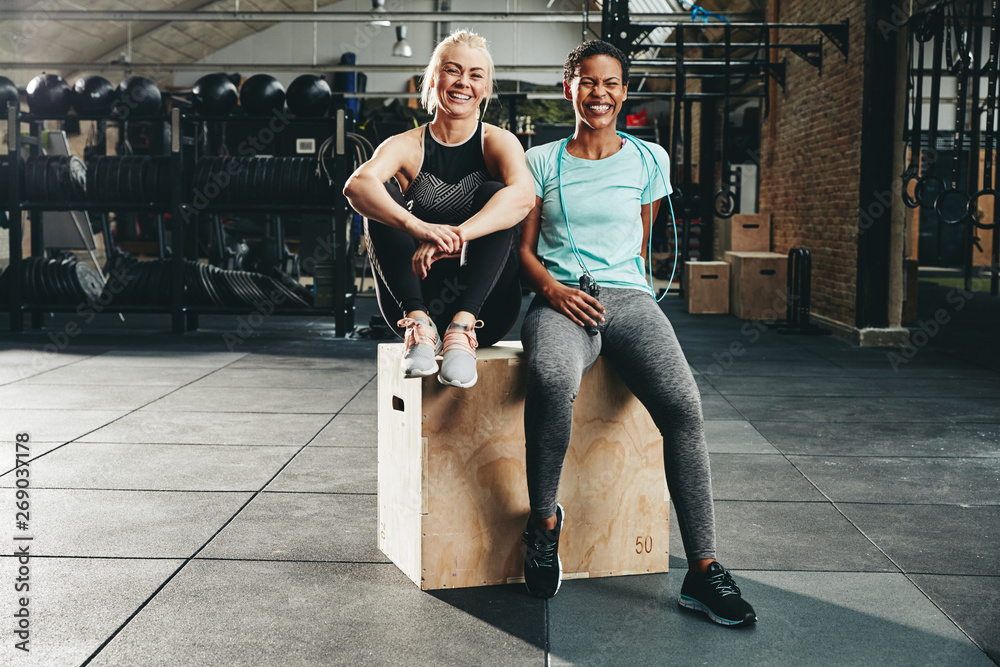 Smiling women sitting on a box together after working out