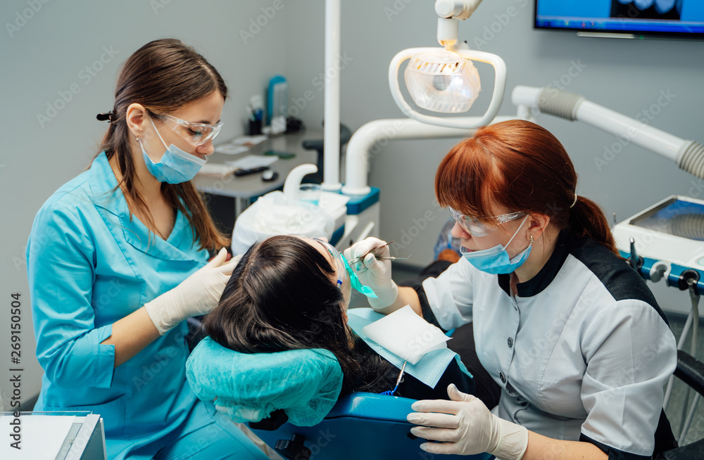 Female dentist and a nurse in masks and protective glasses treating patients teeth. Doctor stomatol