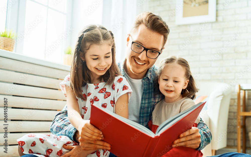 father reading a book to his daughters