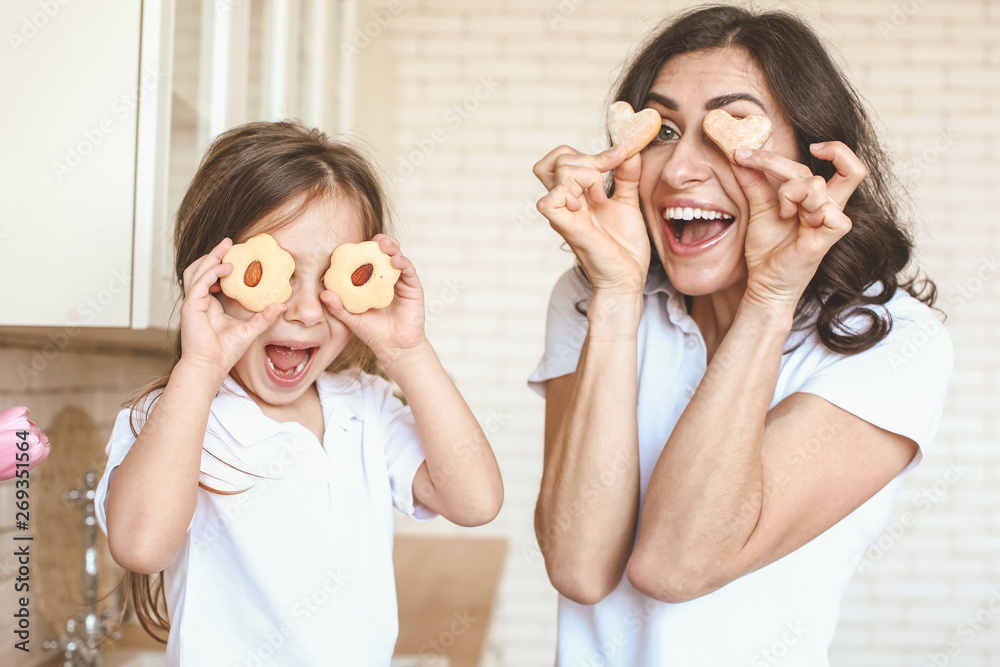 Happy mother and daughter with tasty cookies having fun in kitchen at home