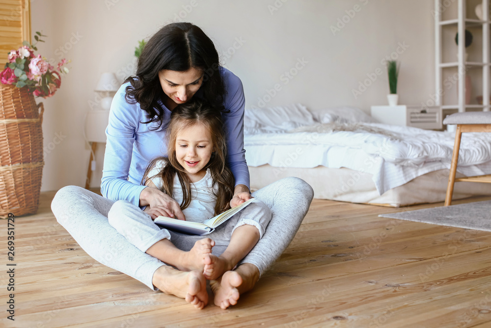 Happy mother with daughter reading book at home