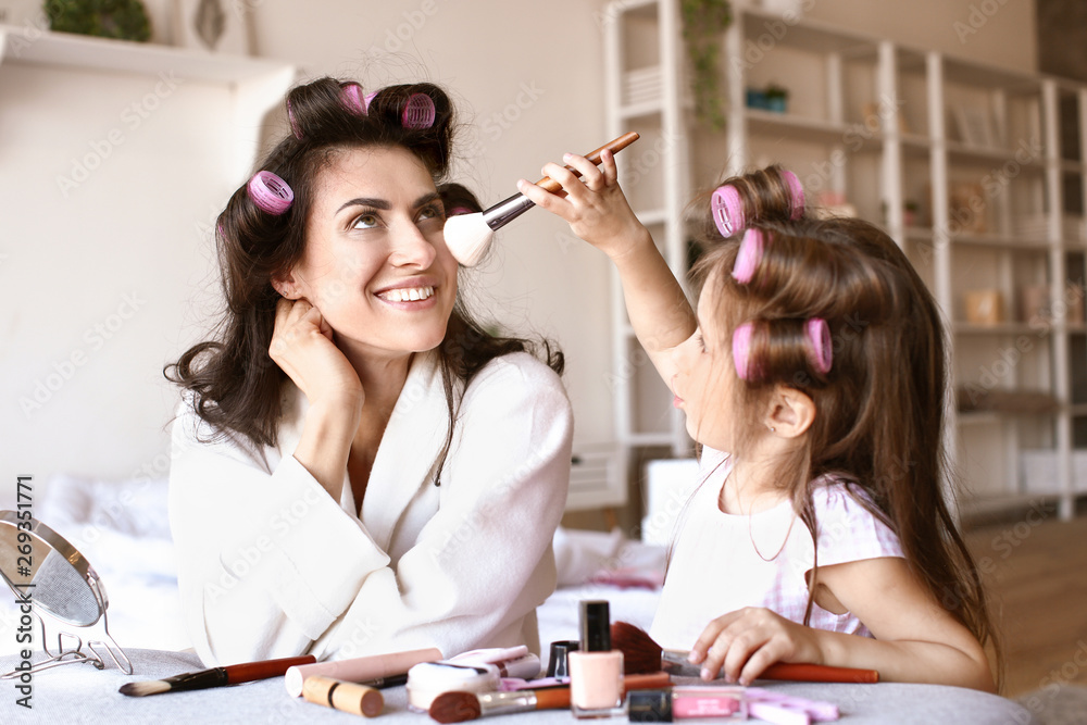 Mother with cute daughter doing makeup at home