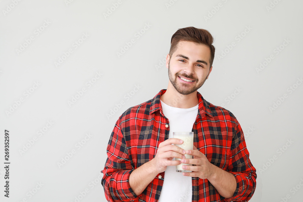 Handsome man with glass of tasty milk on light background