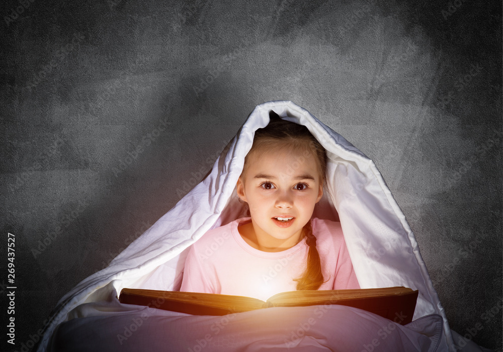 Little girl reading book in bed