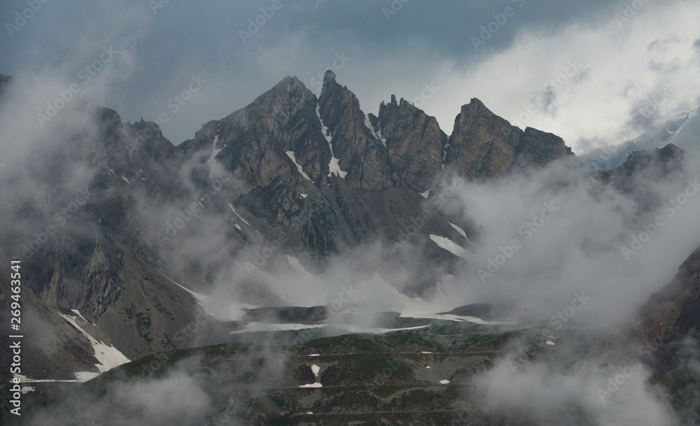 AERIAL: Flying towards rocky mountains high in the sky among the white clouds.