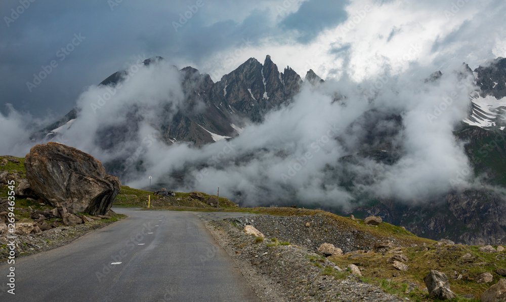 Empty asphalt road runs past the rocky mountains covered in the morning fog.