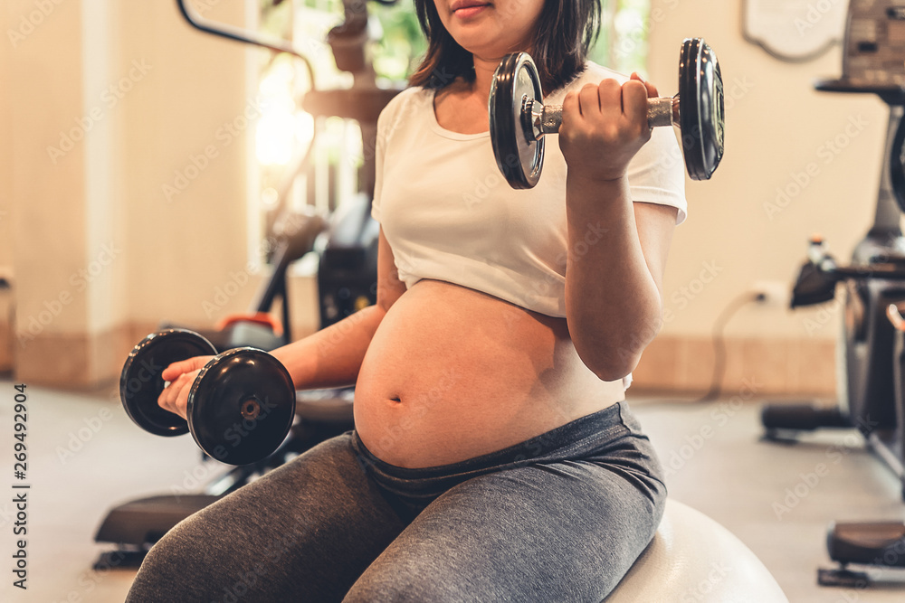 Active pregnant woman exercise in fitness center at yoga room. The young expecting mother holding ba