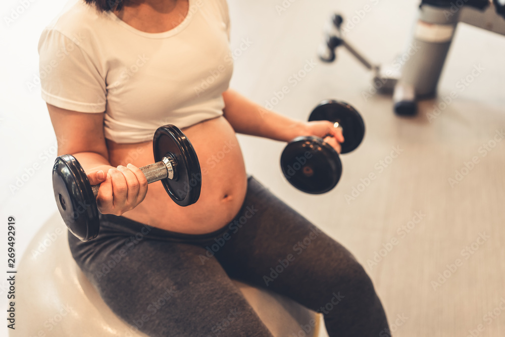 Active pregnant woman exercise in fitness center at yoga room. The young expecting mother holding ba