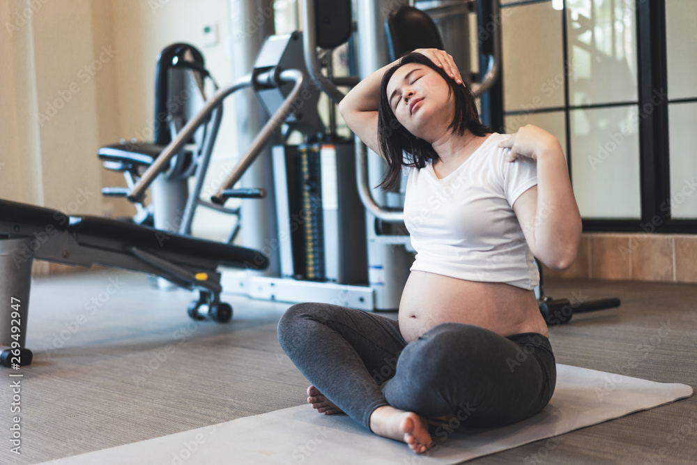 Active pregnant woman exercise in fitness center at yoga room. The young expecting mother holding ba