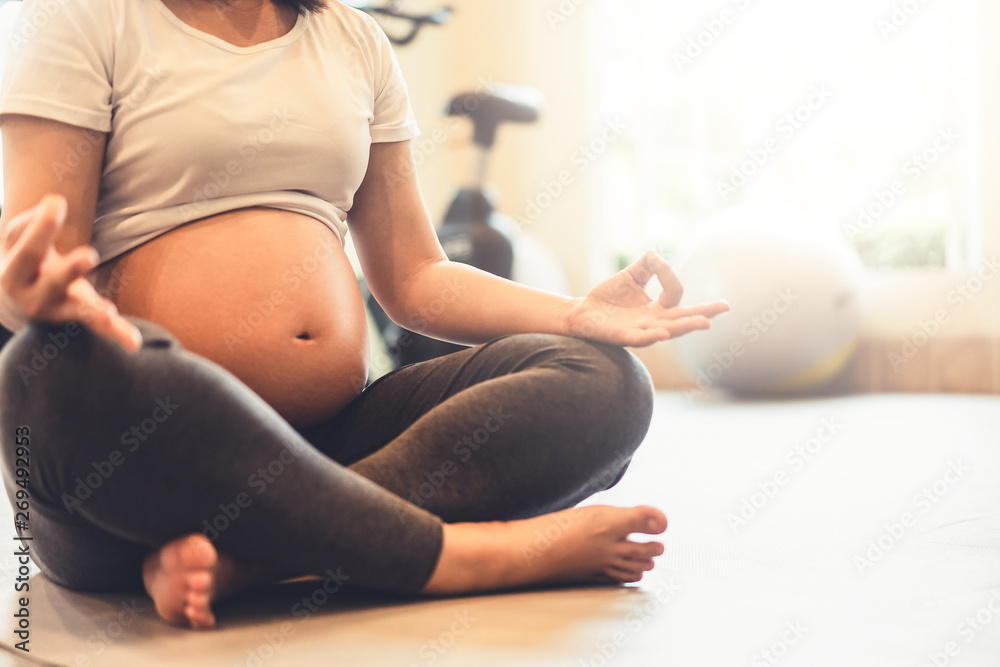 Active pregnant woman exercise in fitness center at yoga room. The young expecting mother holding ba