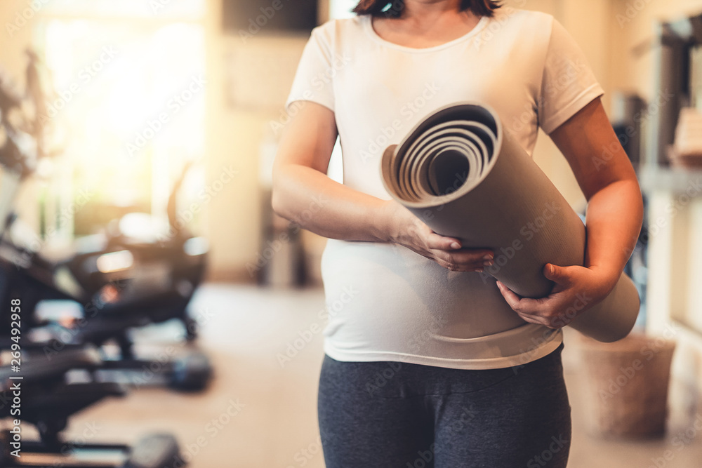 Active pregnant woman exercise in fitness center at yoga room. The young expecting mother holding ba