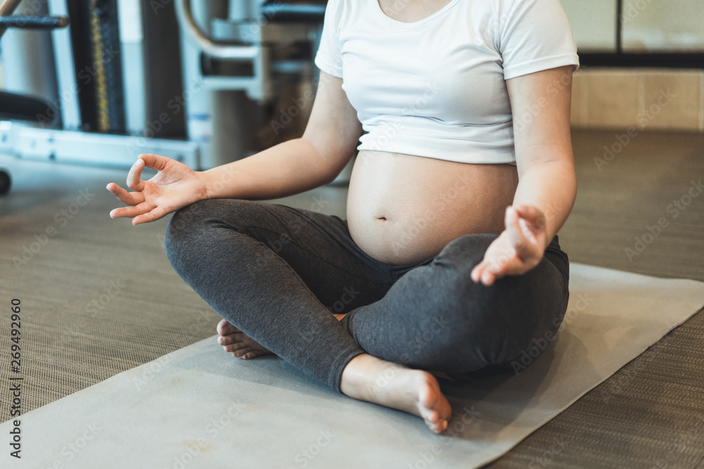 Active pregnant woman exercise in fitness center at yoga room. The young expecting mother holding ba