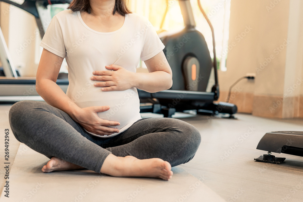 Active pregnant woman exercise in fitness center at yoga room. The young expecting mother holding ba