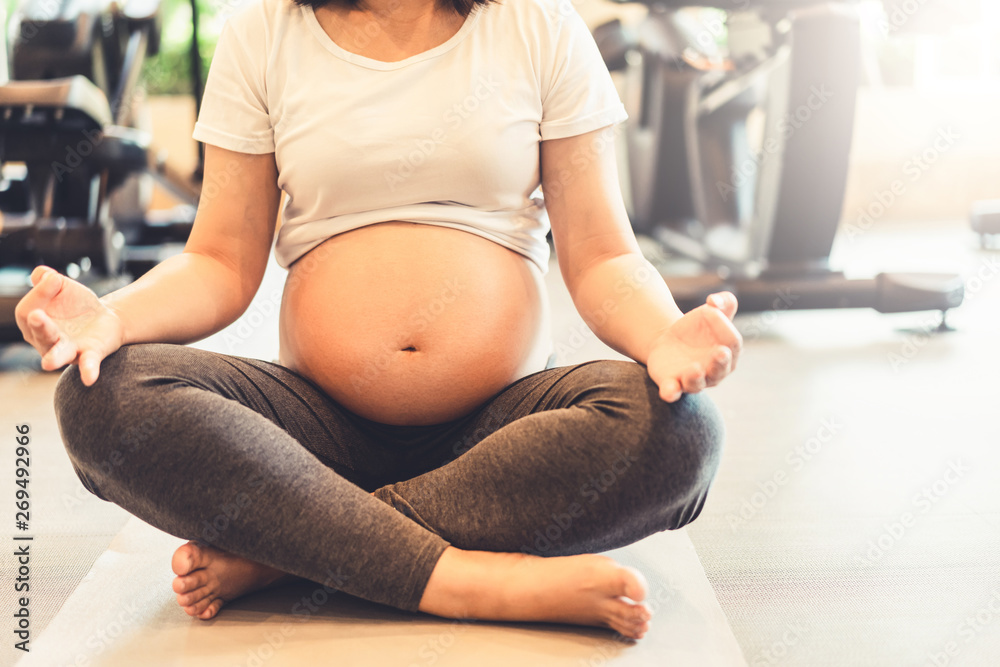 Active pregnant woman exercise in fitness center at yoga room. The young expecting mother holding ba