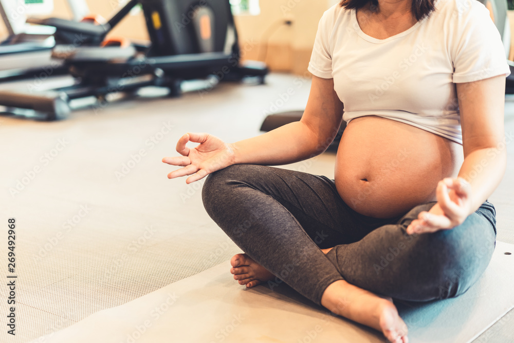 Active pregnant woman exercise in fitness center at yoga room. The young expecting mother holding ba