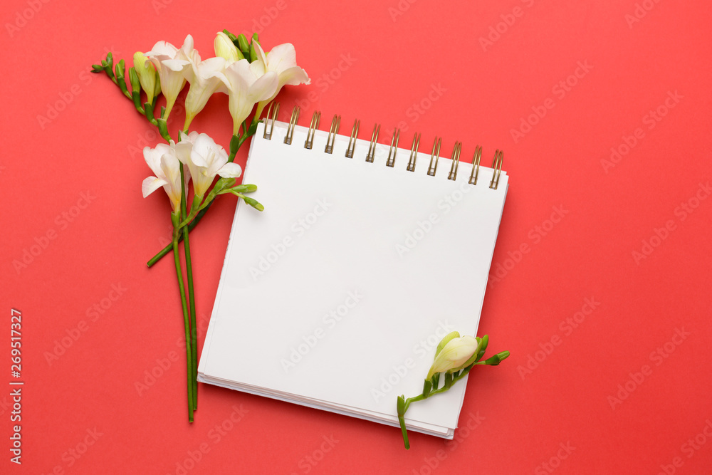 Beautiful freesia flowers and notebook on color background