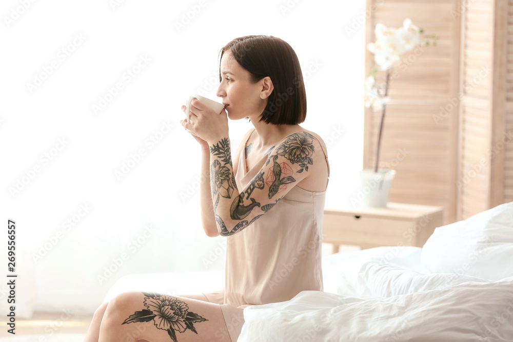 Morning of beautiful tattooed woman drinking coffee in bedroom