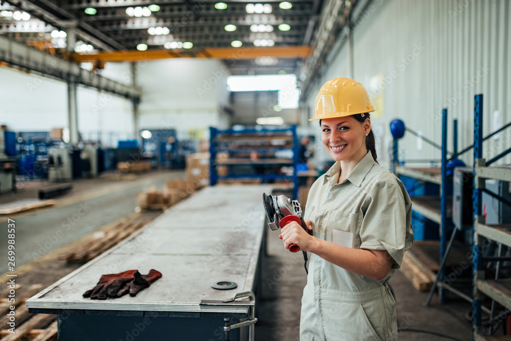 Portrait of a female factory worker holding grinder, smiling at camera.