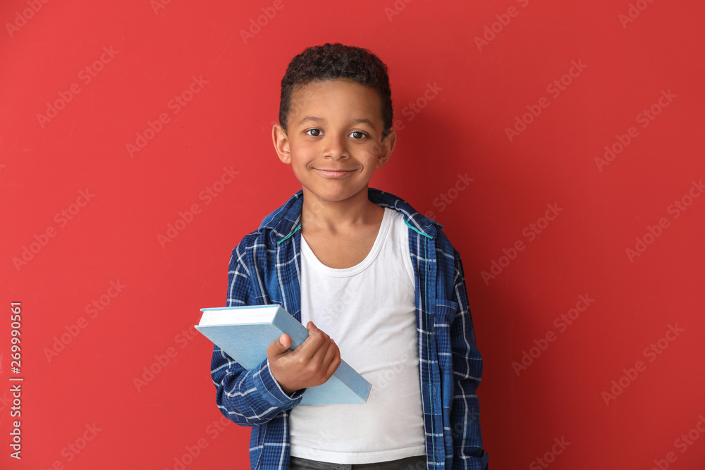 Cute African-American boy with book on color background