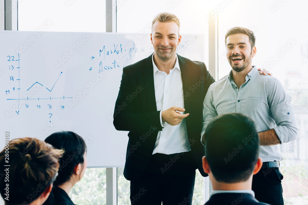 Smiling adult men in formal suits standing near whiteboard doing presentation for coworkers in moder