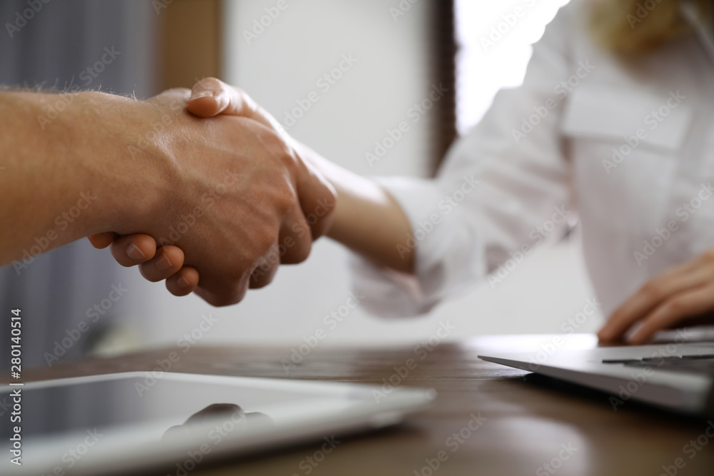 Business partners shaking hands at table after meeting in office, closeup