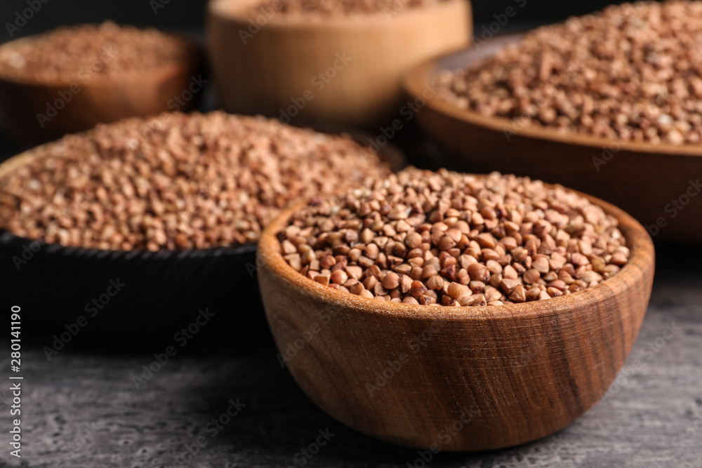 Wooden bowls full of uncooked buckwheat on grey table