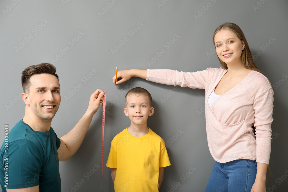 Parents measuring height of their son near grey wall