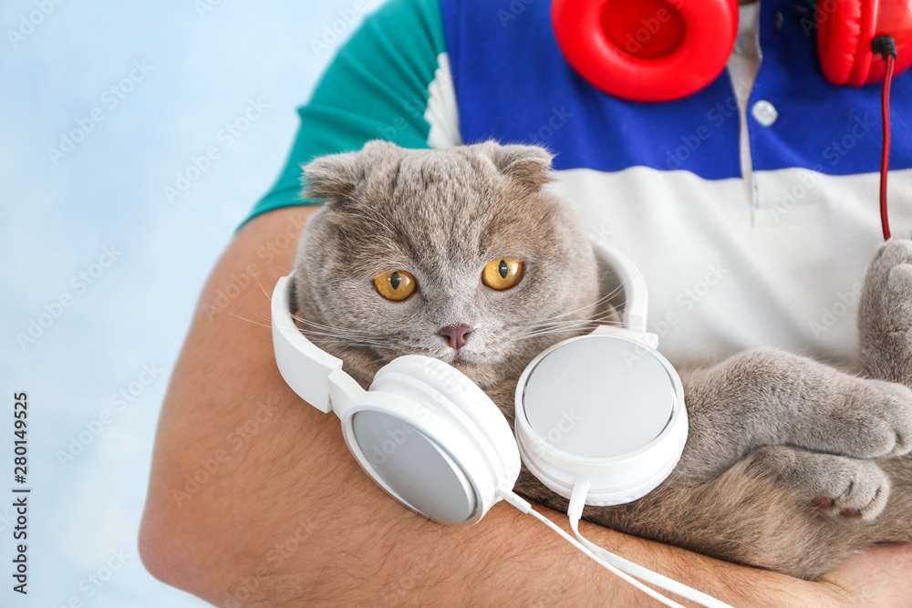 Young man and his cute funny cat with headphones on color background