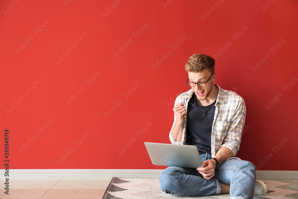 Happy young man with laptop sitting near color wall