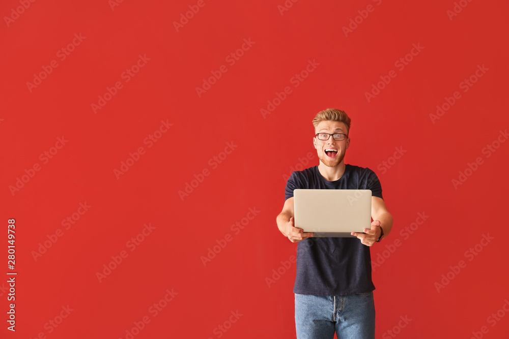 Happy young man with laptop on color background