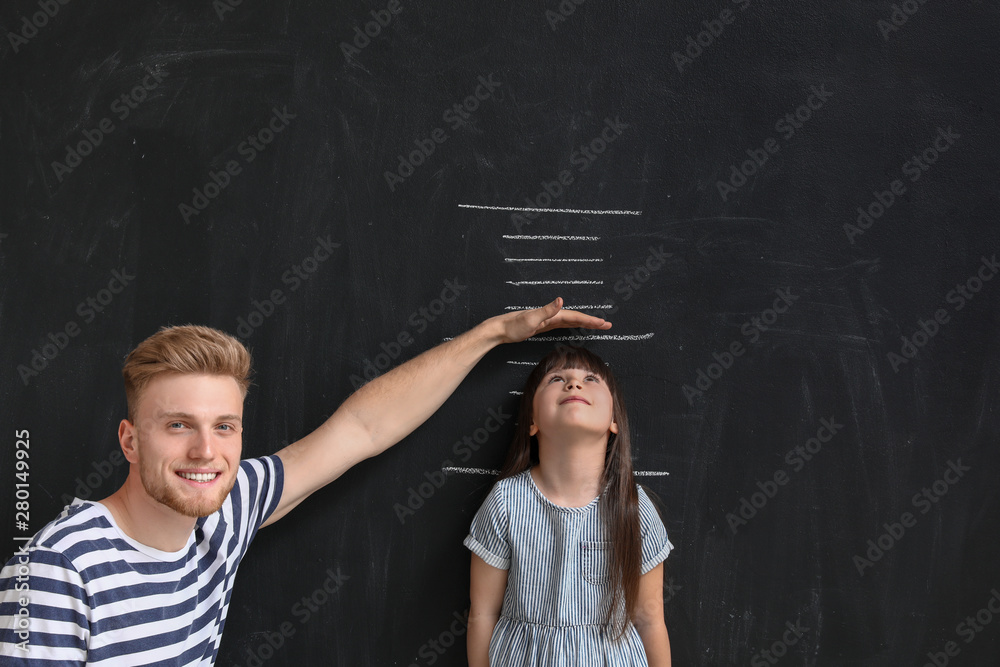 Father measuring height of his little daughter near wall with marks