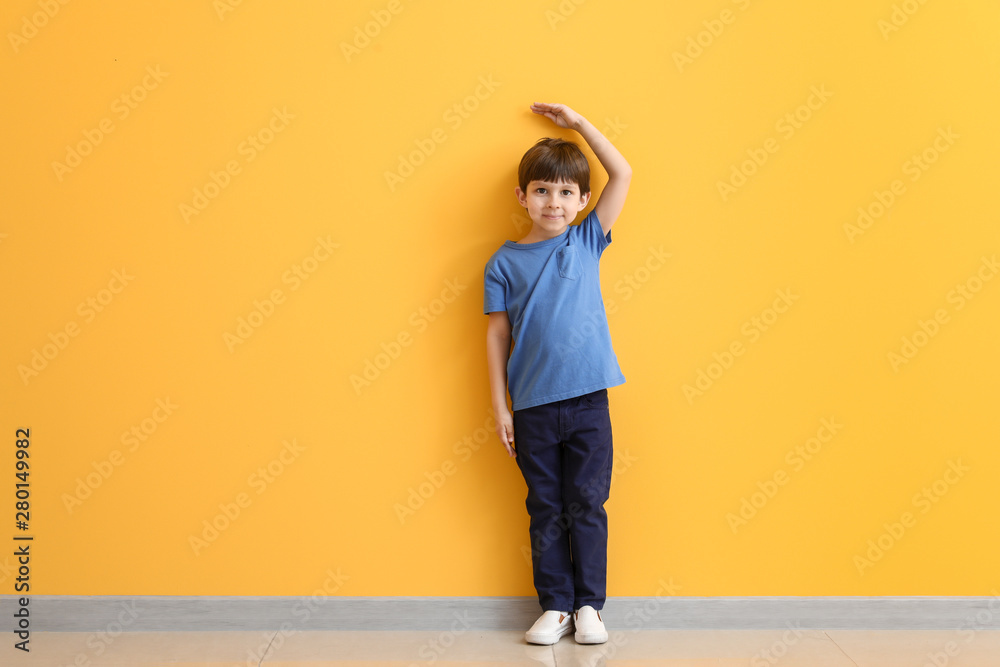 Cute little boy measuring height near color wall